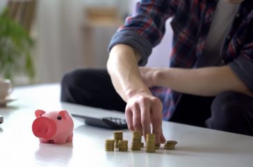 Man taking coins from table near empty piggy bank, last savings, poverty concept