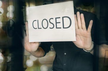Man putting closed sign in window in shop. Late at night in city.