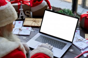 Santa Claus using laptop computer mock up white screen sitting at table.