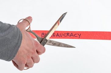Male hand cutting through bureaucracy red tape with scissors iso